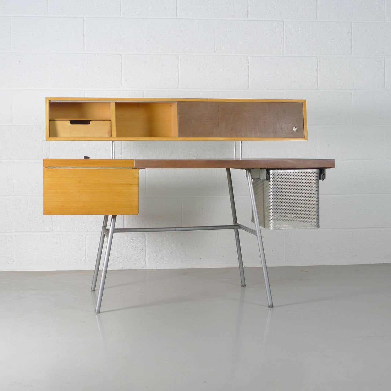George Nelson for Herman Miller, USA, circa 1948. Home office desk, model #4658. Steel frame with perforated steel file holder, leather and wood top. Floating back with sliding doors in leather to reveal original wooden shelving and