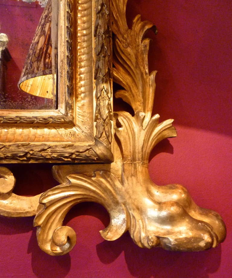 A magnificent and rare Italian large giltwood mirror, Rome c.1750. The arched plate surrounded by a concave gadrooned frame, elaborately decorated with foliate scrolls and a crest incorporating a carved mask of “The Green Man”. The base with