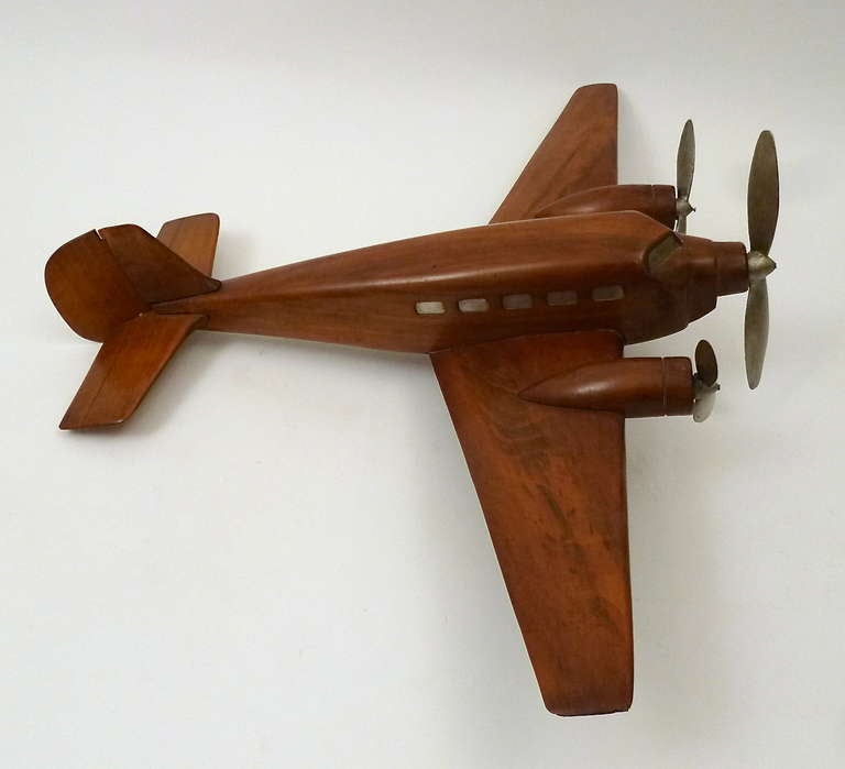 A very decorative and finely carved two engine French model aeroplane c1950. The fuselage and engines are made from solid walnut, with the propellers and windows of the vessel painted silver. The Aeroplane is raised on two rotating wheels.