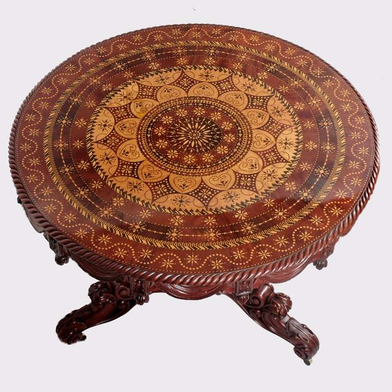 A very fine continental highly carved mahogany centre table with a maple and rosewood top exquisitely inlaid with geometric designs, above a carved swag frieze supported by an ornate triform base, profusely carved with C scrolls and acanthus, on