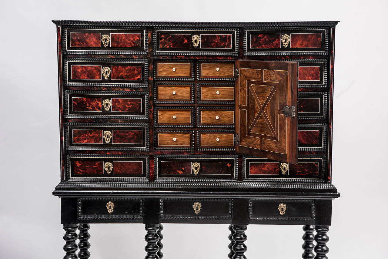 A stunning 17th century Flemish tortoiseshell and ebony veneered collector’s cabinet, circa 1680. With a central door inlaid with ebony, revealing interior drawers in tulipwood, kingwood and walnut, on a later 19th century ebonized stand with bobbin
