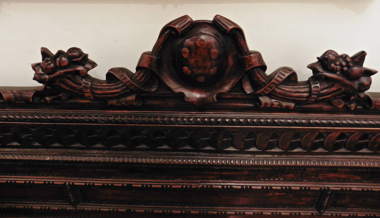 A very fine carved walnut Cassapanca with a strigulated frieze to the front of the base, flanked by foliate carved pedestals supporting shaped armrests faced with carved winged grotesques. The backrest centered with a cabochon shield flanked by