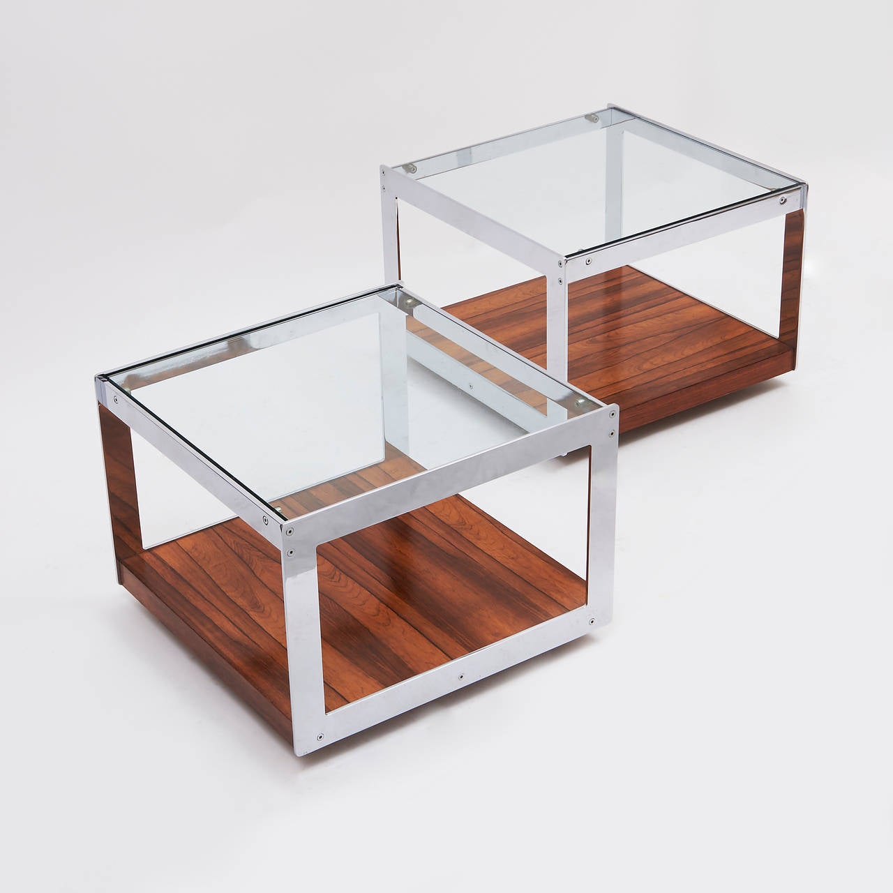 A very stylish pair of English coffee tables and a bar cart, designed by Richard Young for Merrow Associates, circa 1970. Each with a glass topped, chromed steel frame supported by a rosewood veneered base, on original castors. Sold as a set, or
