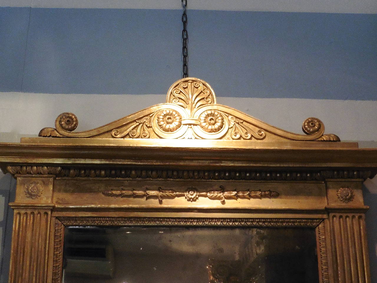 An elegant Italian neoclassical giltwood mirror with an Anthemion pedimented crest above the orginal bevelled mirror plate, flanked by fluted pilasters, terminating in paw feet, circa 1820.