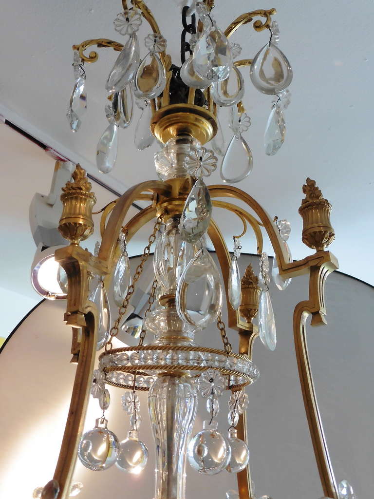 French gilt bronze and crystal Neoclassical eight light chandelier, circa1900. The gilt bronze frame centered by a decorative column surmounted and flanked by plaquette cut drops, spires and small finials. The scrolled gilt bronze arms supporting a