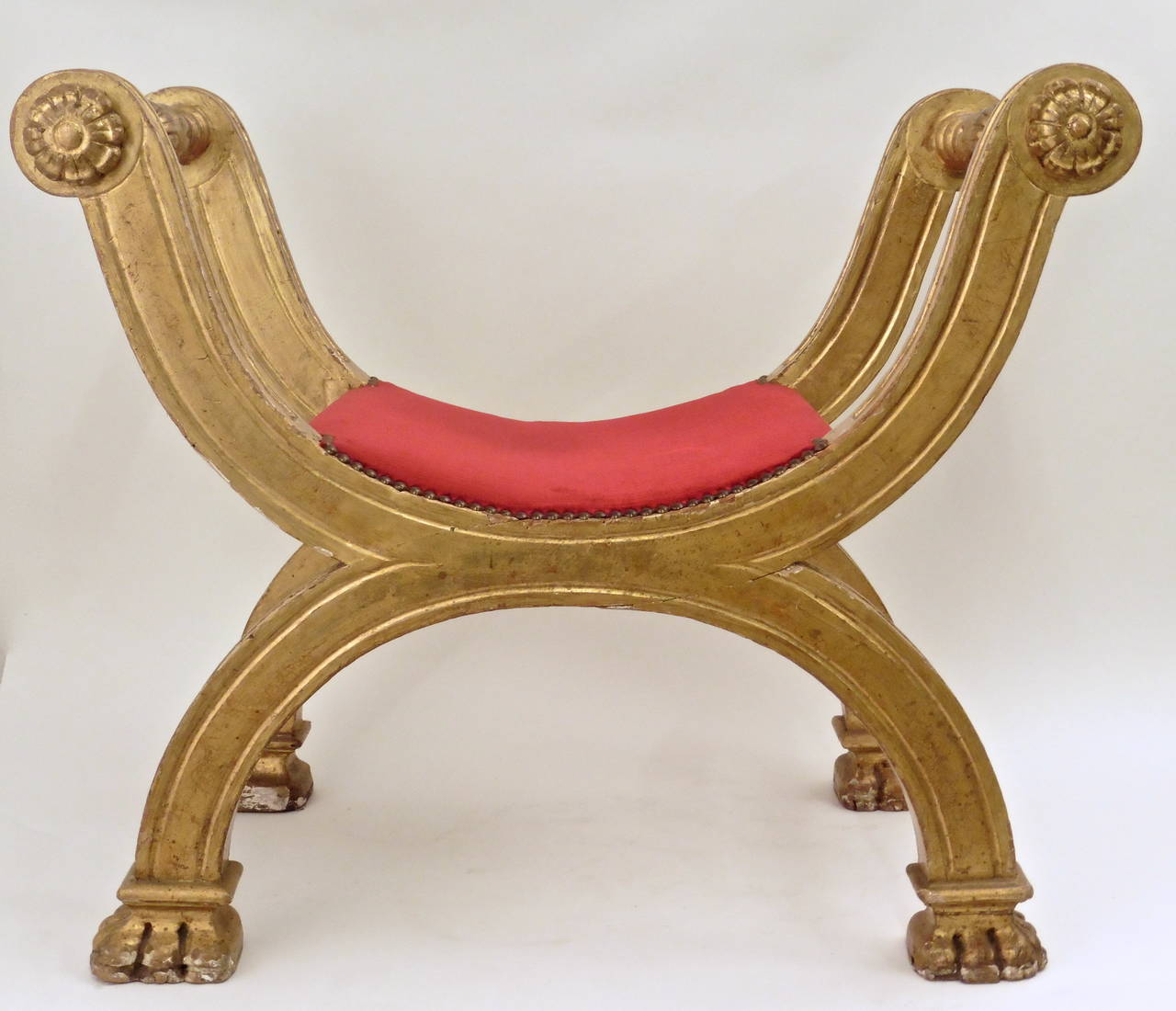 Pair of Roman giltwood X-frame stools, Italy, circa 1820. 

The legs terminate with paw feet and the armrests have foliate decor. The seats are upholstered in red velvet.
