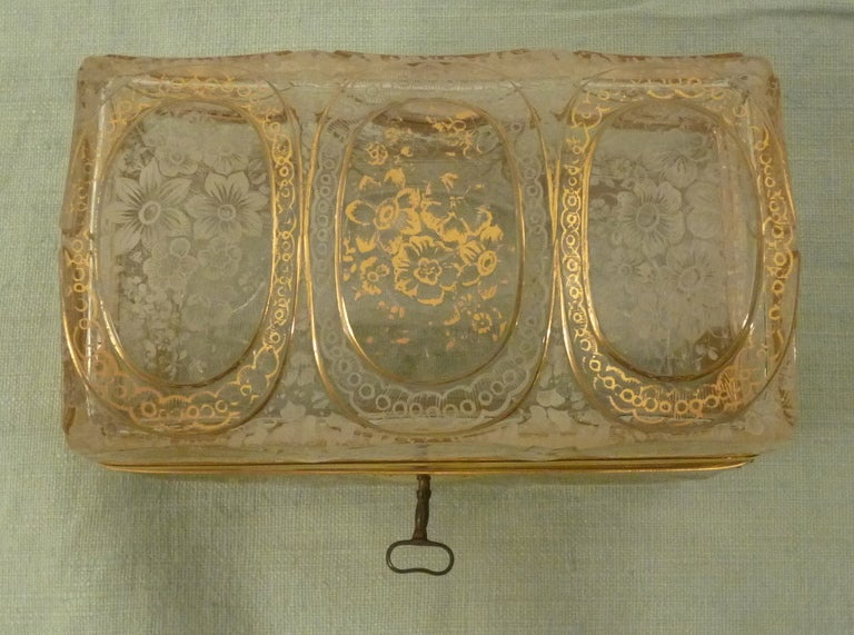 This beautifully etched glass casket has intricate detailing throughout, typical of Bohemian glass which is famous for its cut and engraving. Its floral deign is accentuated by a  gilt overlay on alternate panels giving the impression of scales, or
