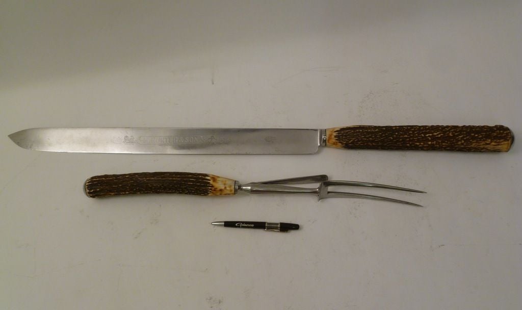 Shop display oversize carving knife and fork in steel with antler handles, with makers mark for Michael Hunter & son, Sheffield c.1900.<br />
The carving Knife bearing one of the firms listed trade marks “FUERTE”.<br />
<br />
Carving Knife: 35.5