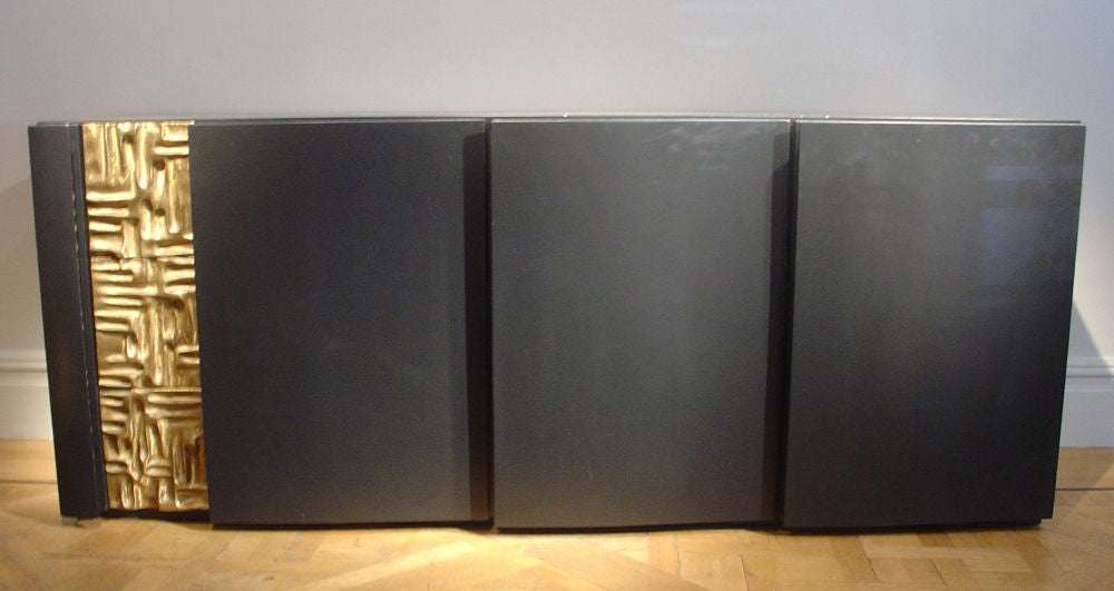 An Ebonised Three Door Cabinet with Inset Cast Bronze Panel; the Doors Opening to Reveal Shelves and Drawers.