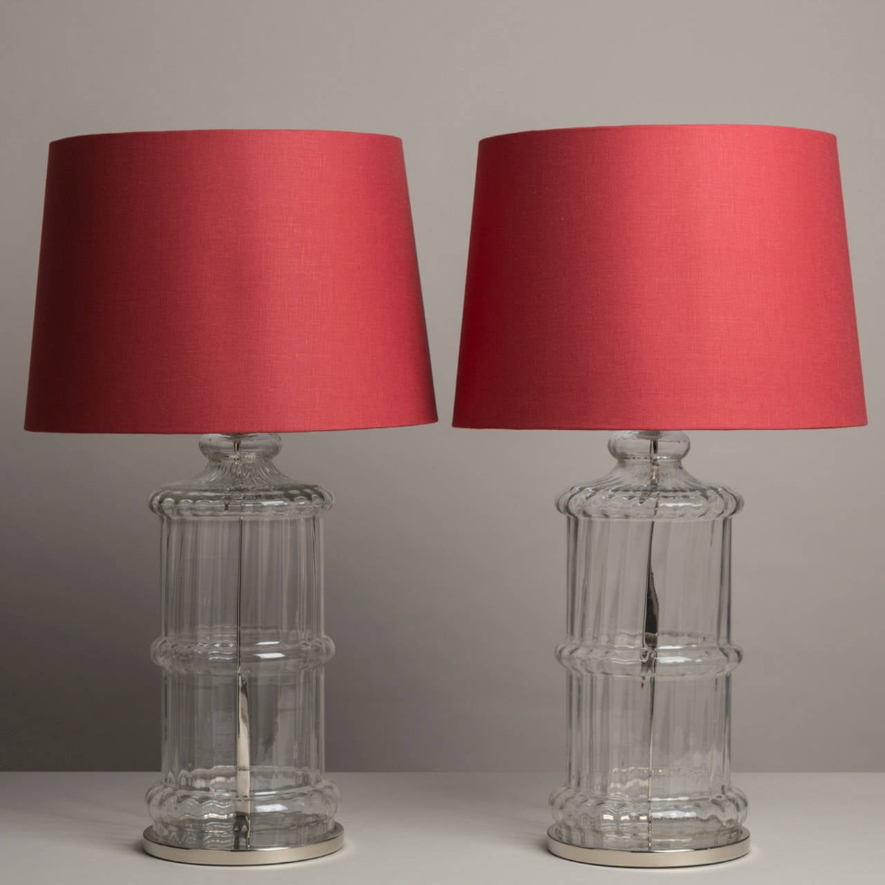 A pair of moulded ribbed glass table lamps with nickel plated detail, 1970s
Accompanied with red linen shades.
