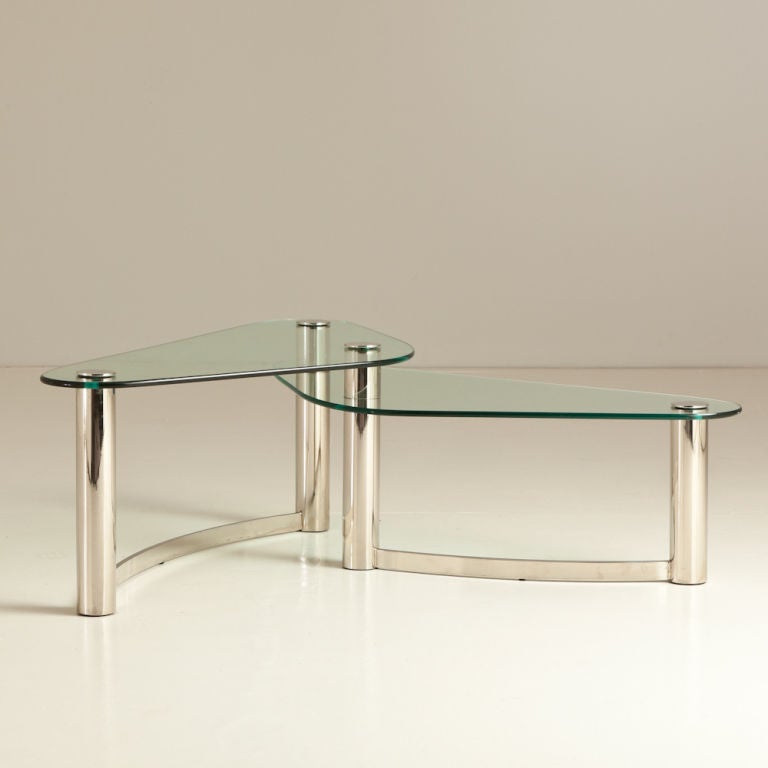 A 1970s tubular nickel and glass asymmetrical two tier overlapping coffee table  
Each of the two pieces of glass measures 113cm wide X 53.5cm deep 
The two tiered heights are 35.5cm and 46cm- 
Width of coffee table at widest point is 137.2cm
