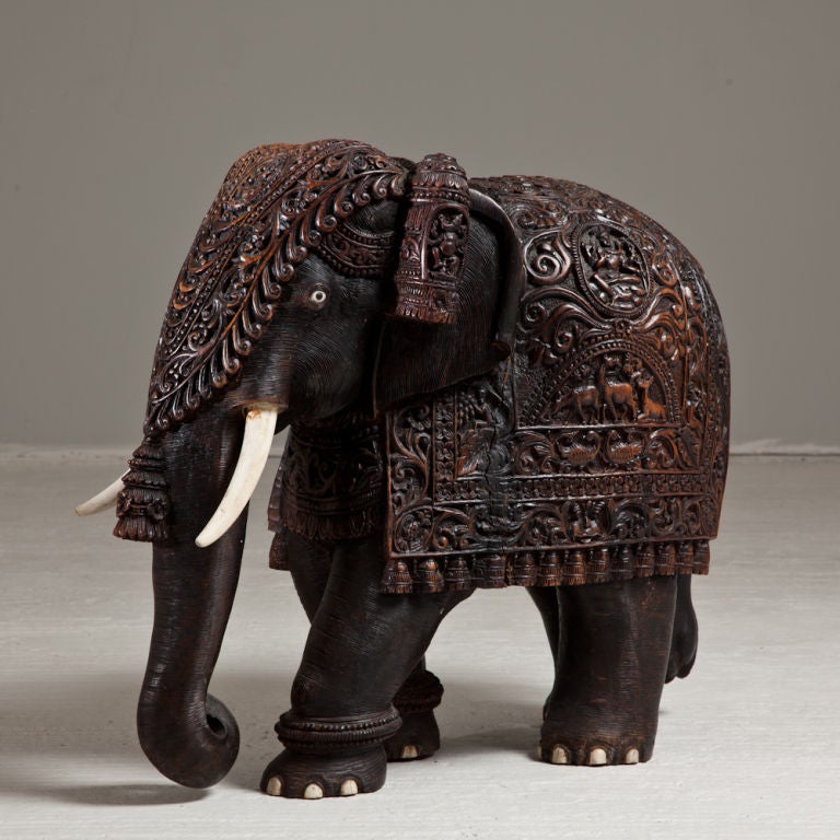 A Superb Mid 19th Century Teak Indian Elephant depicted with an intricately Carved Ceremonial Sardozi and Head Dress and with Carved Bone Tusks