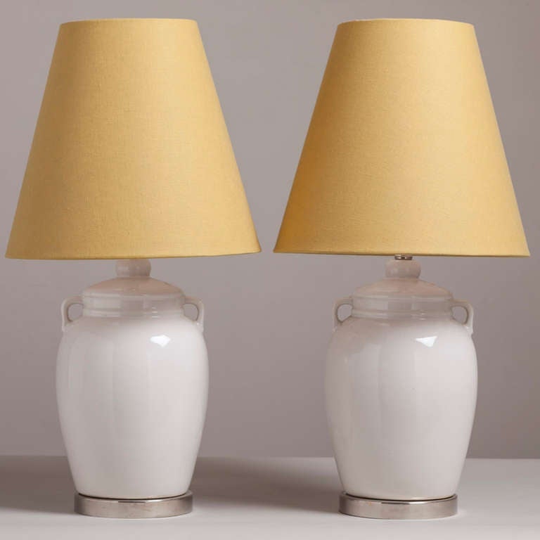 A pair of white ceramic urn shaped table lamps on nickel-plated mounts and accompanied with yellow linen shades. 1960s.