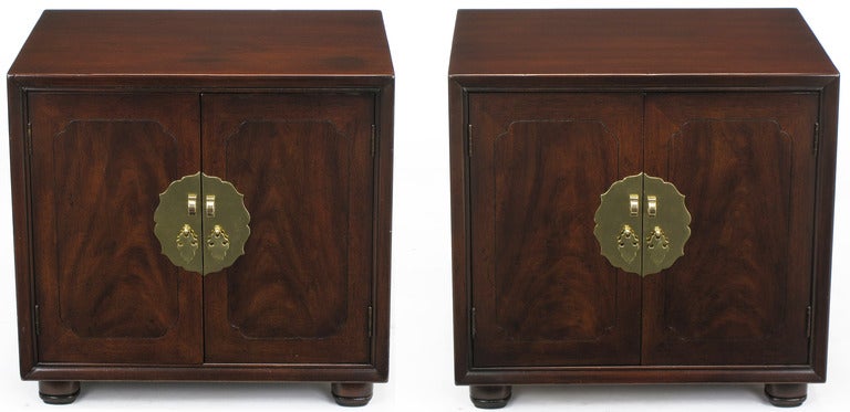 Asian influenced pair of walnut cube tables with incised border to figured walnut doors. Large brass escutcheons with spear tip form brass drop pulls and U-shape brass lock adornment.
Open center with single shelf and internal electrical outlet