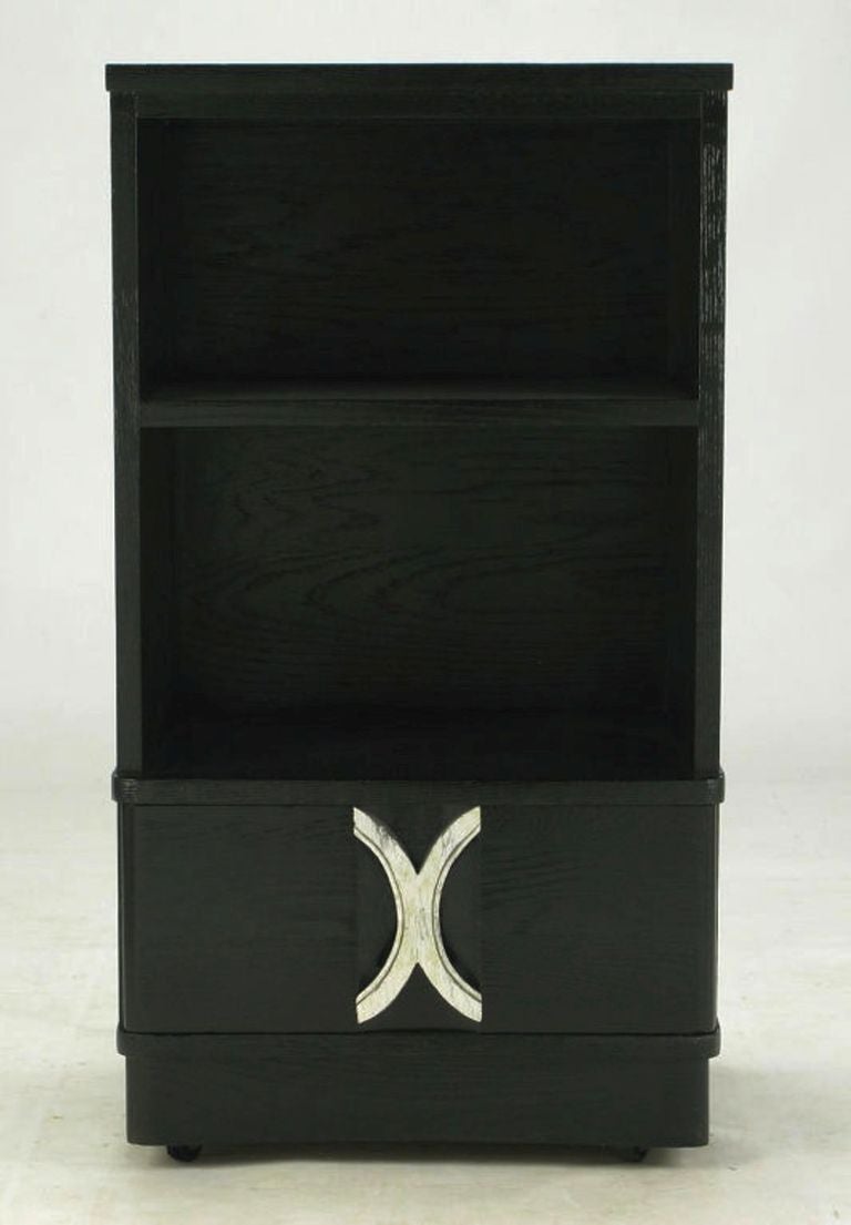 Beautiful black lacquer over a deep grained oak with a single drawer featuring silver leafed carved wood X pull. Large open compartment with a single shelf and curved front plinth base with original casters.
