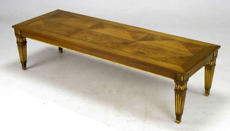 An outstanding walnut coffee table from Baker featuring a diamond patterned parquetry inlay top, with parcel gilt fluted Louis XVI style legs.