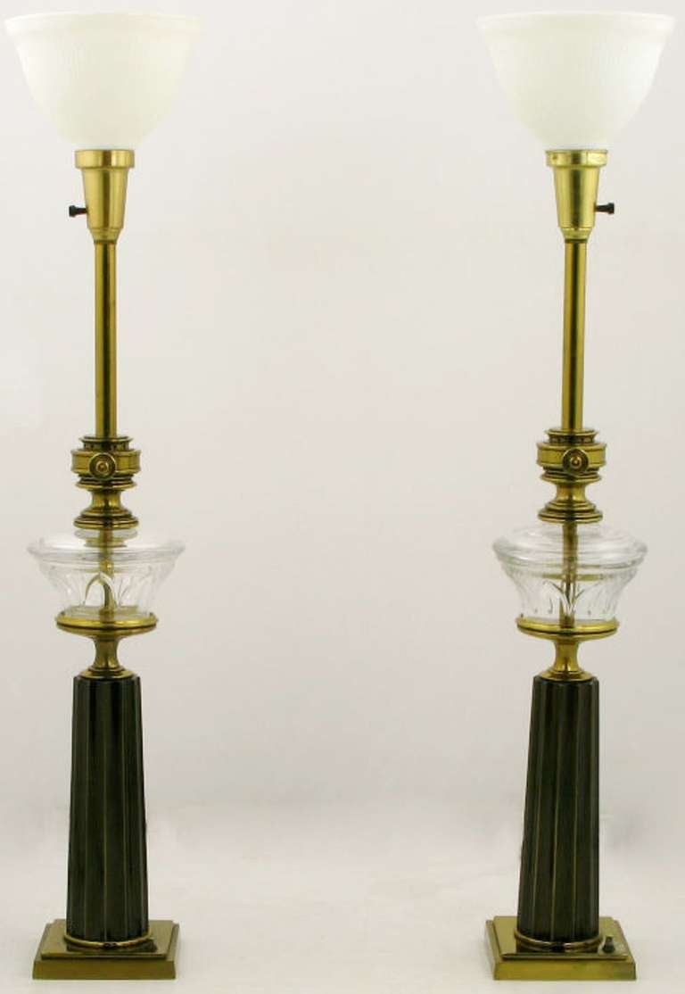 Pair of oil-lamp style table lamps with fluted brass columns on stepped plinth bases with push button on/off switches. Bodies have clear, cut glass bowls with ornamental brass valve detail. Original milk glass diffusers, sold sans shades.
