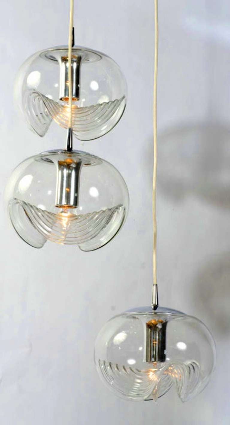Suspended by white cords from a large chrome ceiling canopy, three blown glass globes are held in place with chrome fitters and sockets. The clear glass globes have a crimped and rippled design. Cord lengths can be shortened, as required by ceiling