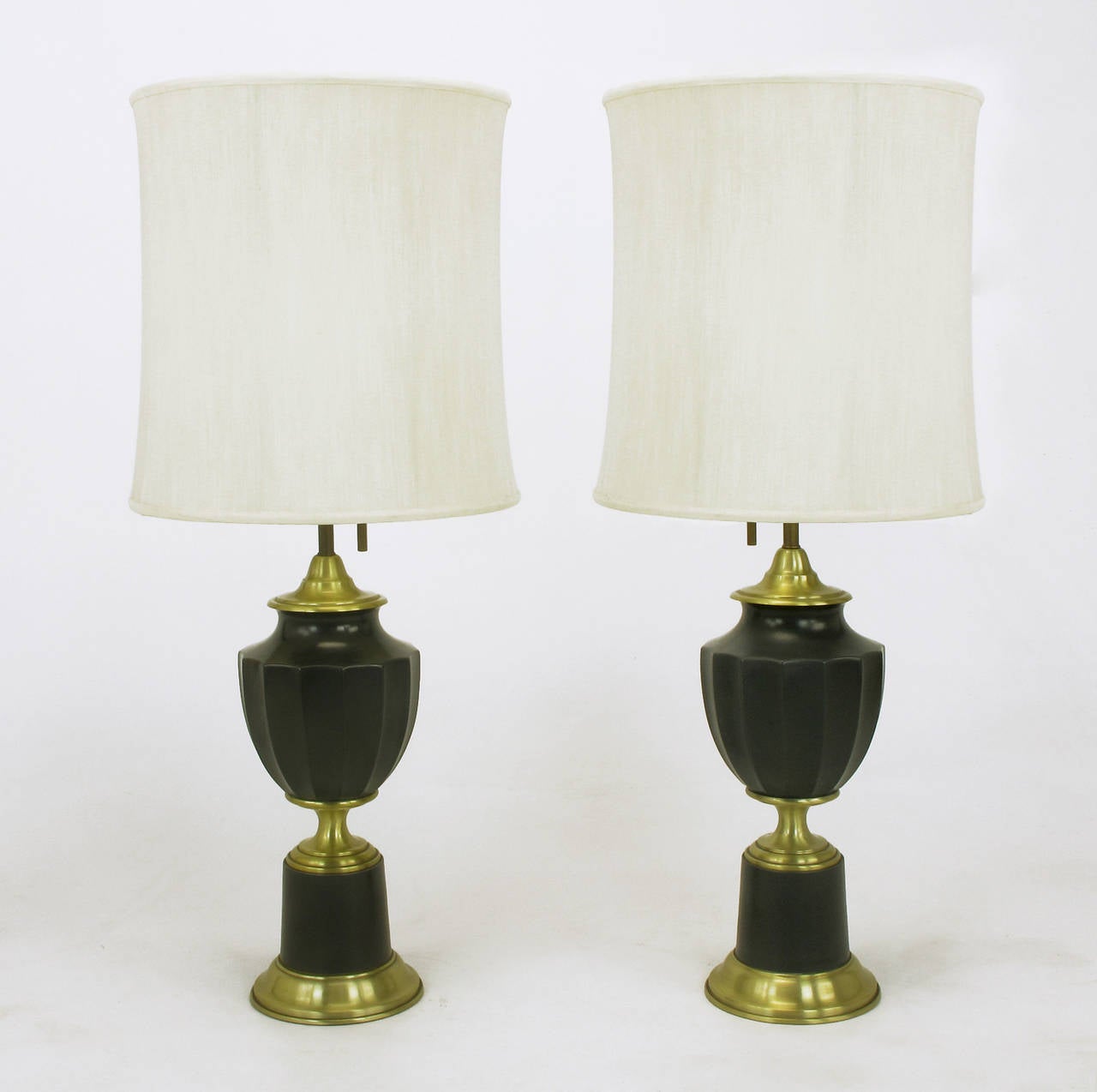 Elegant pair of neoclassical table lamps from Lightolier with spun brass caps, risers and base. Also, dark green lacquered metal fluted urn body and cylindrical pedestal appear as stone. Lightolier three way socket housing in white lacquer with