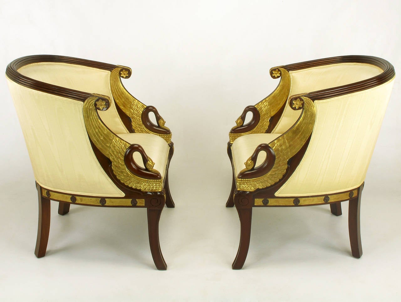 Pair of Maitland Smith Empire revival parcel-gilt bergeres with swan head and wing detail. Mahogany frames with cream silk moire upholstery. Reeded back rail, gilt apron with rosettes, gilt acanthus leaf details to the arms and legs.