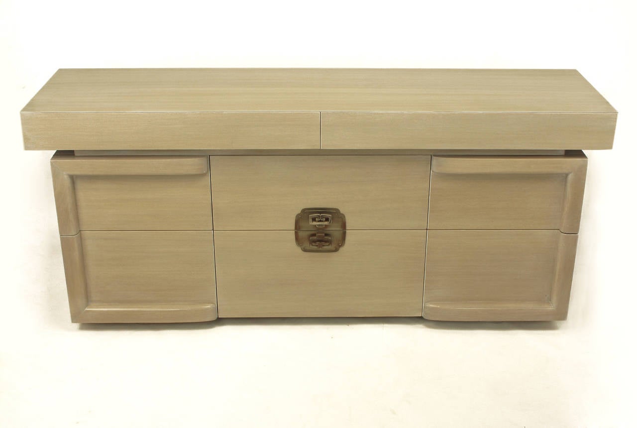 Eight-drawer dresser with recessed casters hidden beneath half oval feet and new driftwood glazed finish. Patinated nickel over copper centre medallion with a pair of cast pulls. Other pulls are integral to the sides of or underneath each drawer.