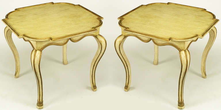 Pair of neoclassical parcel gilt over ivory glazed wood side tables from Los Angeles based manufacturer to the trade, Minton-Spidell. Exaggerated cabriole legs with carved feet, scalloped apron with a recessed top. Finished in an antiqued ivory