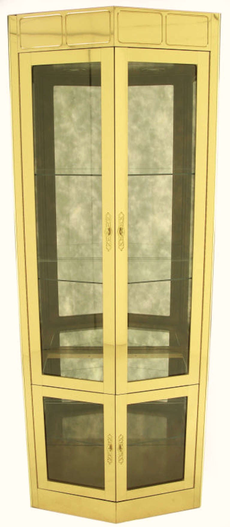 Pair of Mastercraft pentagonal brass over wood four door vitrines. Taller top compartment has two glass shelves. Lower compartment has a single glass shelf. Tops are illuminated with two incandescent recessed lights and a dimmer switch. Pierced