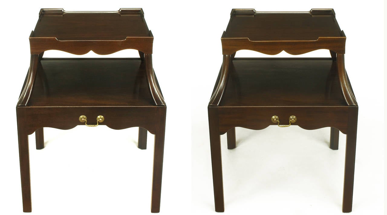 Pair of elegantly understated and restored mahogany two-tiered end tables attributed to Kittinger Furniture Buffalo NY. Scalloped aprons to all sides and both tiers, four gallery corners to the top tier, five sided legs, pull-out surface with