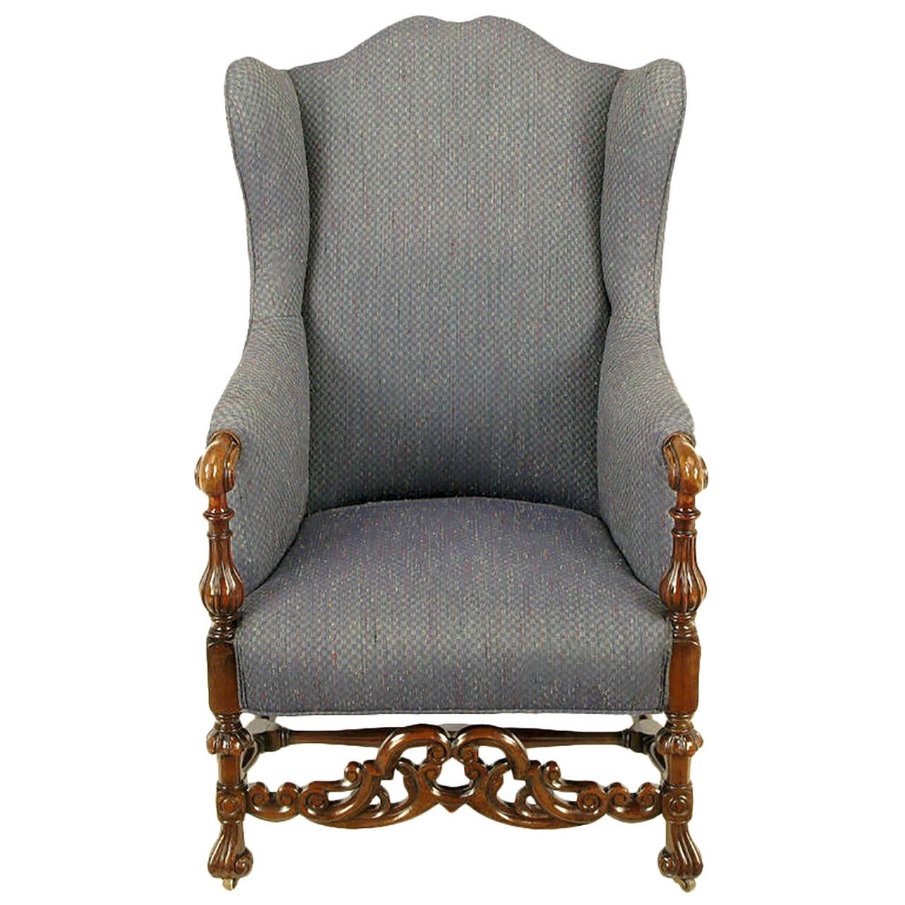 Italian 19th century style wing chair. Heavily carved front apron and arms through the front legs. Carved middle and side stretchers and back legs. Upholstered in a charcoal blue wool silk blend. Muted checked pattern heathered with red, light blue