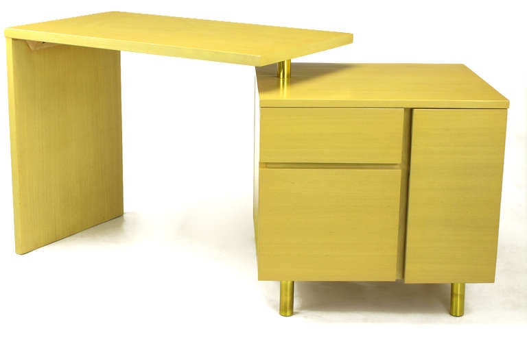 Articulated writing table with L shaped writing surface and a stationary cube. Writing surface pivots via a brass sleeve over a steel post located in the top of the cubed piece. Features include two drawers with one being a file drawer and a shelved