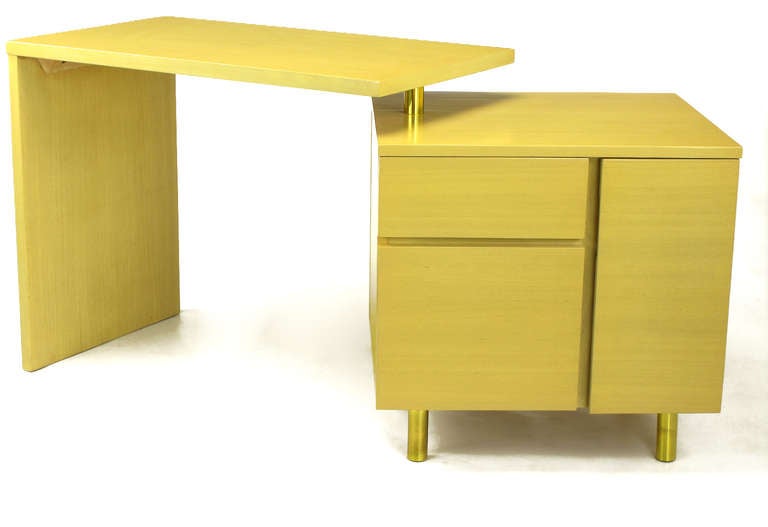 Articulated writing table with L shaped writing surface and a stationary cube. Writing surface pivots via a brass sleeve over a steel post located in the top of the cubed piece. Features include two drawers with one being a file drawer and a shelved