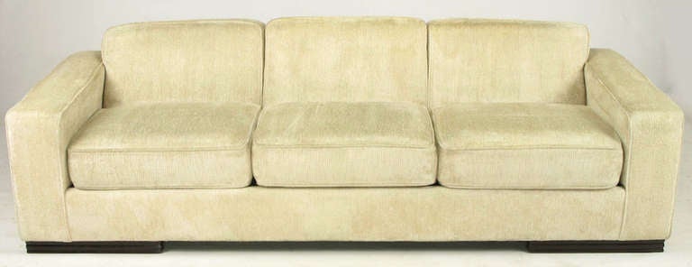 Larry Laslo for John Widdicomb art deco revival sofa in cream textured chenille with wide low arms, thick loose cushioned seats and a canted fixed three part back. Four long carved wood feet.