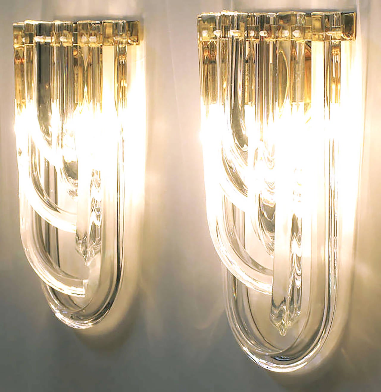 Outstanding and rare pair of Italian bent triangular crystal and brass wall sconces from Venini. One U-shape crystal with offset descending J-shape crystals. Brass demilune frame with two candelabra base light sockets. Multiple pairs available.