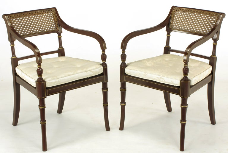 Pair of regency style arm chairs by Kindel Furniture, Grand Rapids Michigan. Carved wood frame with deep oxblood lacquered finish and parcel gilt detail. Seat and back are woven cane.  Off-white damask upholstered cushions.