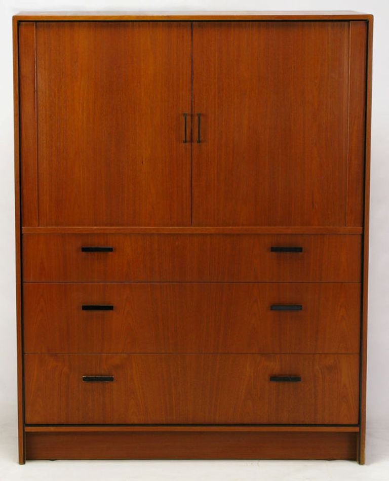 Teak gentleman's dresser or chest, made in Denmark by Falster. Two upper doors with black lacquered metal U-shape pulls open and recess to reveal nine drawers, and two shelf compartments. Three large lower drawers with black lacquered bar pulls.