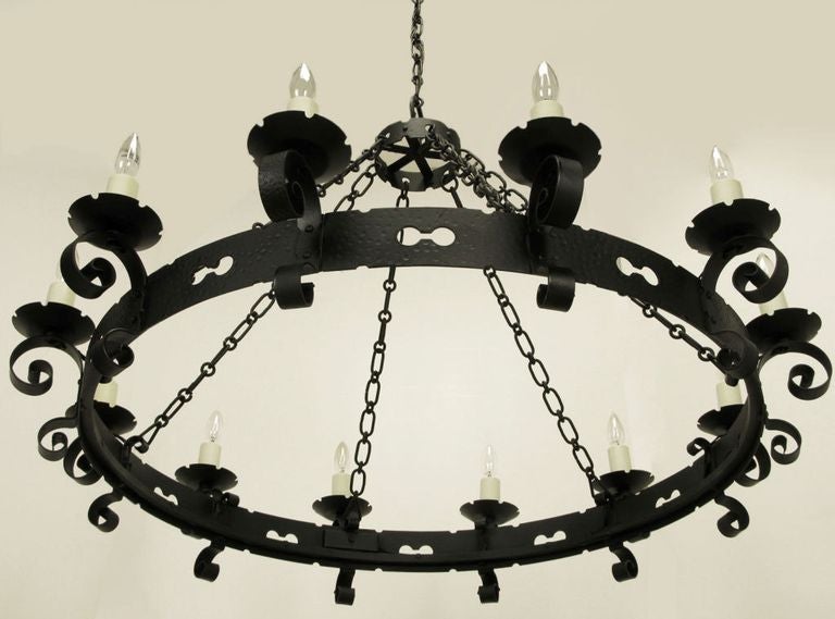 Rare Lightolier Spanish Revival twelve light black wrought iron chandelier. Large pierced and hammered ring with scrolled arms and notched bobeches. Six heavy round and oval link stands of chain meet at another small hammered and pierced ring.
