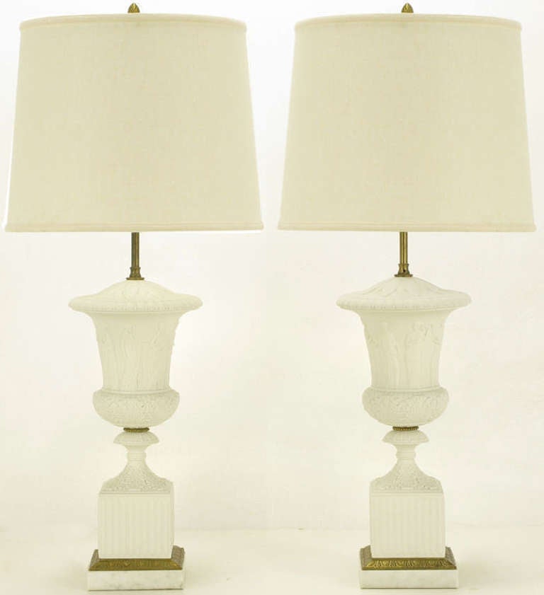 Excellent neo classical white bisque porcelain and cast bronze urn form plinth based table lamps. Acanthus leaf detailing and carved Grecian characters on solid marble urns with fluted cubed plinths and bronze and marble beveled base. Brass stem and
