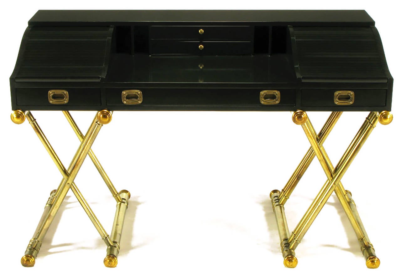 Black lacquered rolltop desk with pair of center top drawers, and compartmented openings behind tambour side sections. Three lower drawers. Brass Campaign style pulls and side handles. Double X-form wood bases in aged silver leaf with gold leaf