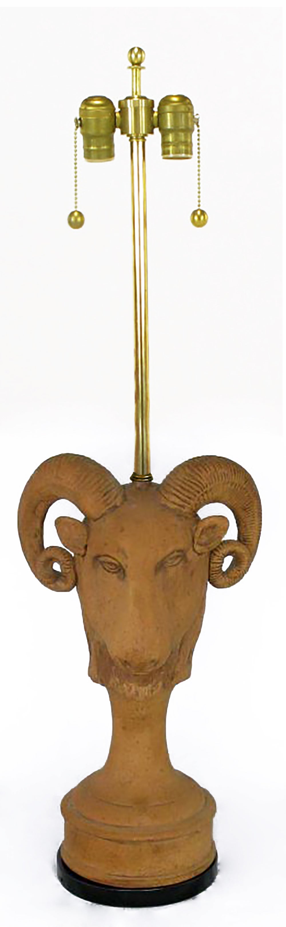 Terracotta table lamps in the form of a full ram's head descending into a pillar and circular base with a black lacquered plinth. Brass stems and double socket clusters, rewired. Label inside states 