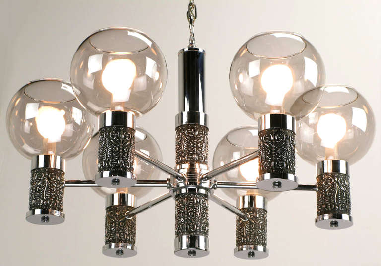 Six-arm chandelier combines chrome-plated metal and cast chrome-plated relief. Cylinders at the center and on each arm are cast resin with an antiqued chrome finish.