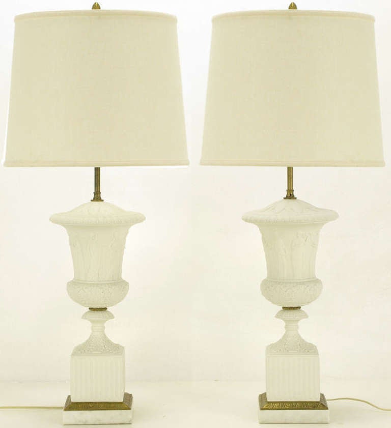 Excellent neo classical white bisque porcelain and cast bronze urn form plinth based table lamps. Acanthus leaf detailing and carved Grecian characters on solid marble urns with fluted cubed plinths and bronze and marble beveled base. Brass stem and