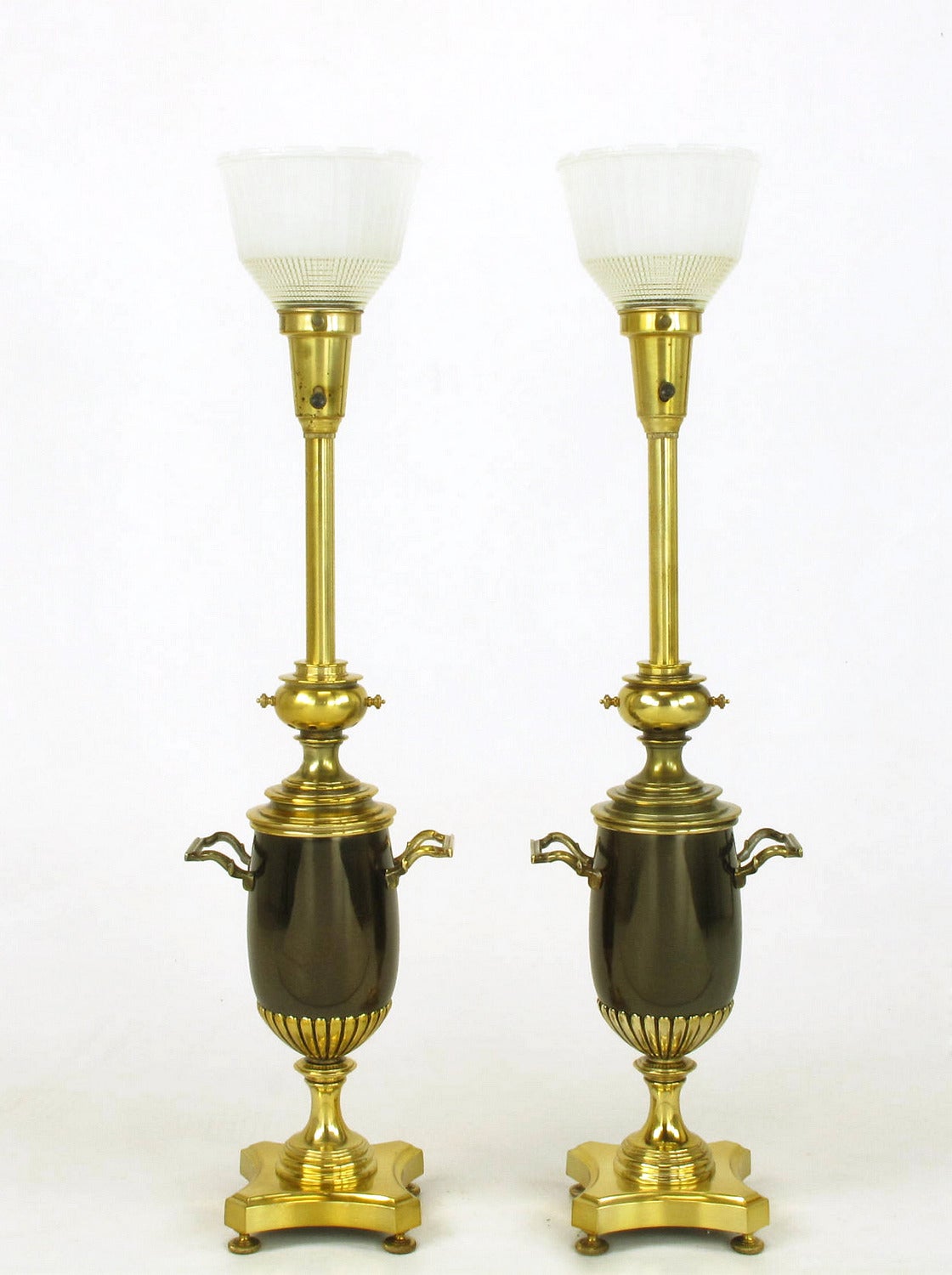 Pair of brass toned silver and bronze urn form table lamps. Urn bodies are bronze with a pair of handles. Reverse quatrefoil footed base, flanged riser, reeded cup, spacers and stem all finished in brass toned lacquer over silver. Manufactured by