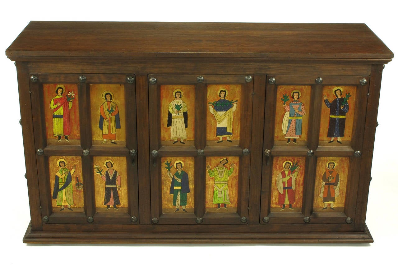 An adaptation of a 16th century hand constructed distressed pine cabinet. The retablo panels depicting the twelve apostles are hand-painted in polychrome over gold leaf. The three door open via hand-forged iron drop pulls with hand-forged iron