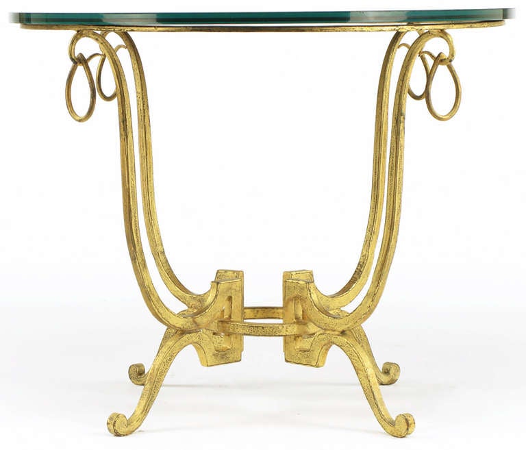 Gilt wrought iron neoclassical base with teardrop rings over open hooks. Four legs are attached to the center top ring and smaller bottom ring. Black glass top is one half inch thick.