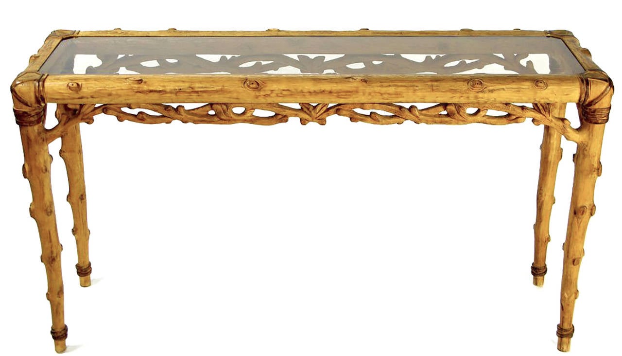 In the style of Mimi London, this elegant console table has a base carved in the likeness of branches and twigs. The detail is exquisite, including carving to simulate rawhide bands lashing the pieces together. A lightly smoked glass top affords