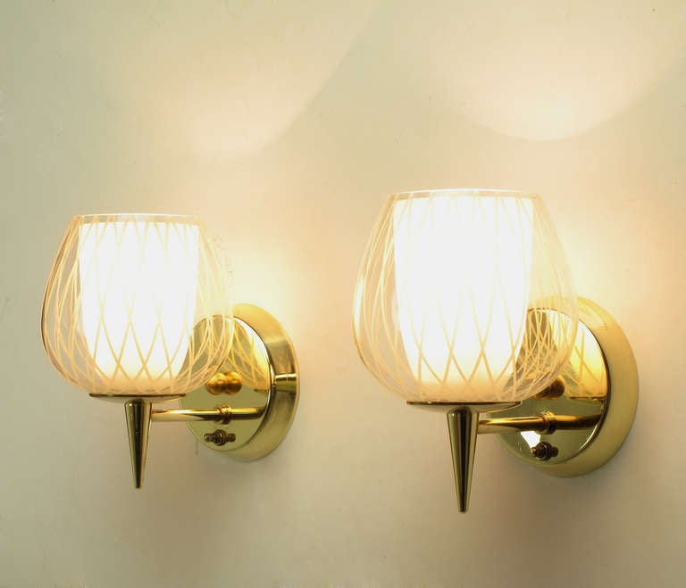 Pair of brass double hurricane sconces by Gerald Thurston for Lightolier. Each solid brass sconce has a double hurricane shade, with the inner shade being a milk glass cup, and the outer shade being an etched, cross hatch on clear, snifter shaped