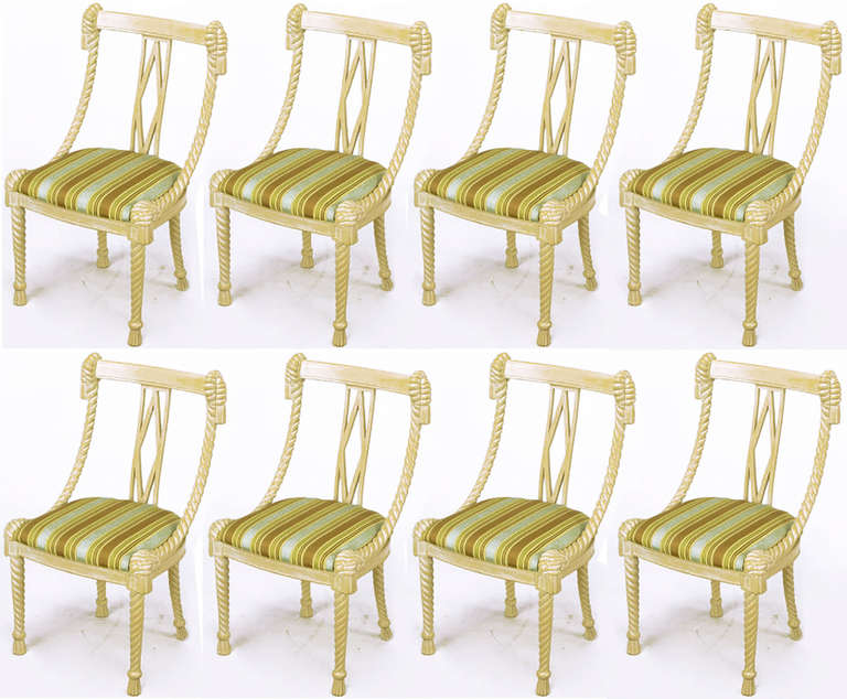 Set of six carved wood dining chairs glazed in an ivory lacquer. Rope form legs and tassel feet with knotted seat corners, swaged sides rise up to knotted and tasselled seat back corners. Open back with elongated diamond shape centre. Striped silk