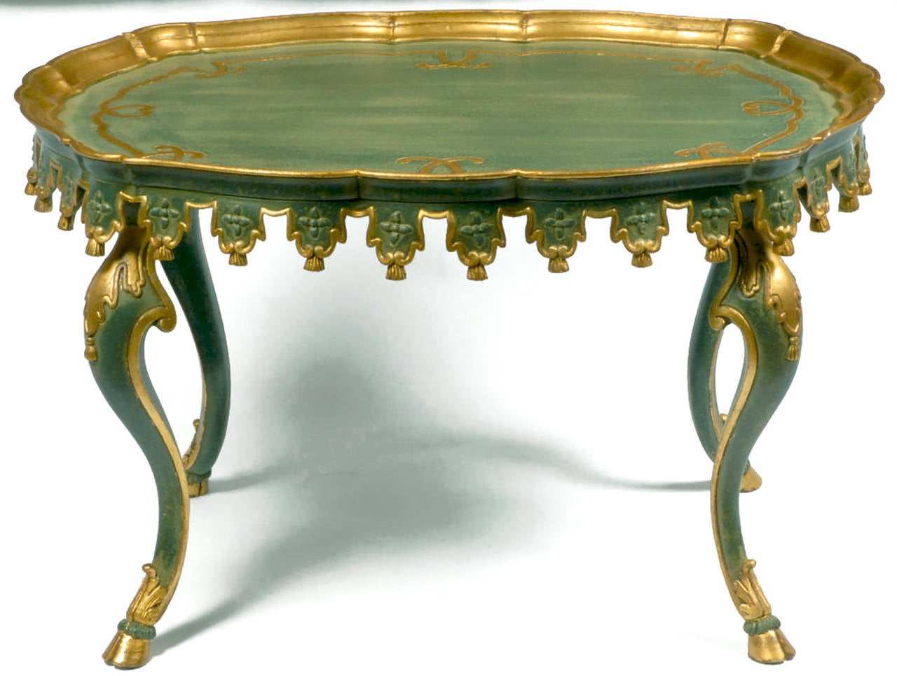 Shaped like a squared-off oval, this table is carved of wood, including tassel ornamentation and hoof feet crested with acanthus leaf trim. Painted a lovely teal blue-green, with an ivory over glaze, it is accented by gilded trim. Marked 