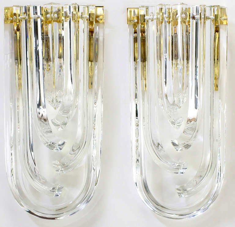 Outstanding and rare pair of Italian bent triangular crystal and brass wall sconces from Venini. One U-shape crystal with offset descending J-shape crystals. Brass demilune frame with two candelabra base light sockets. Multiple pairs available.