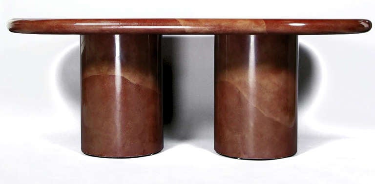 Racetrack oval table on two round cylinder bases, with bullnose edge. Constructed of wood, all covered in plum color faux goatskin lacquer. Some crazing to the lacquered bases that will be restored prior to shipping.